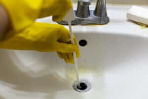 A person is trying to unclog the drain of a sink using plastic disposable snake auger tool